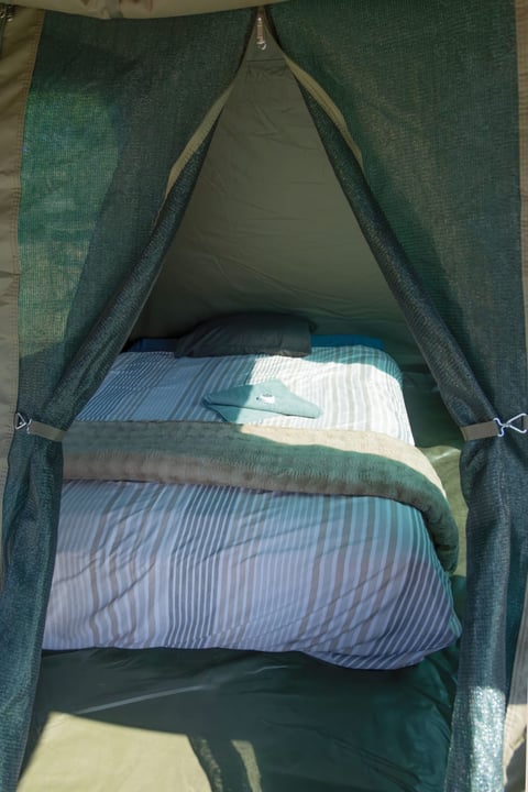Interior view of a green canvas tent with bedding including blue striped pillow and white sheets arranged inside
