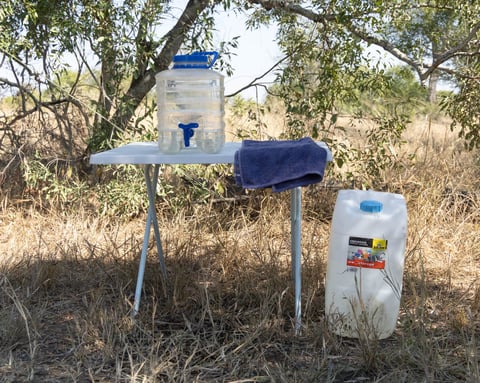 DIY rainwater collection system with plastic containers and blue pipes mounted on pole in dry field with trees