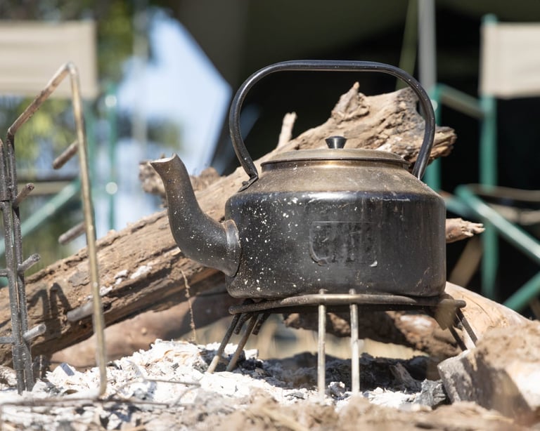 Black kettle on camping stove over fire with wood and rocks in outdoor camp setting
