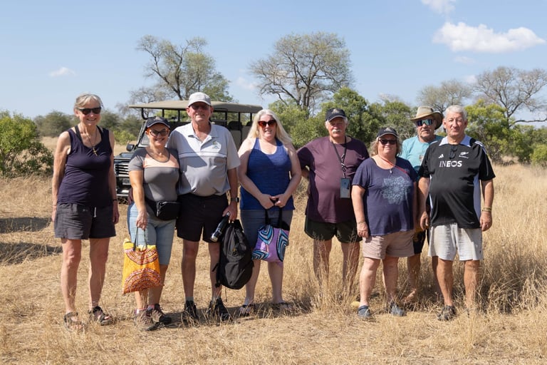 Group of nine tourists standing together on safari in an African savanna with sparse vegetation and trees in background